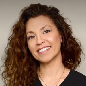 Uśmiechnięta kobieta o długich, kręconych brązowych włosach patrzy w obiektyw.