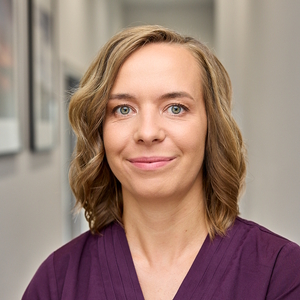 Kobieta o jasnych kręconych włosach w fioletowej bluzce patrzy w obiektyw.