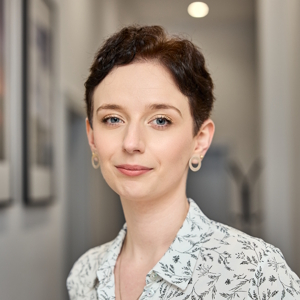 Kobieta o krótkich ciemnych włosach w jasnej koszuli patrzy w obiektyw.