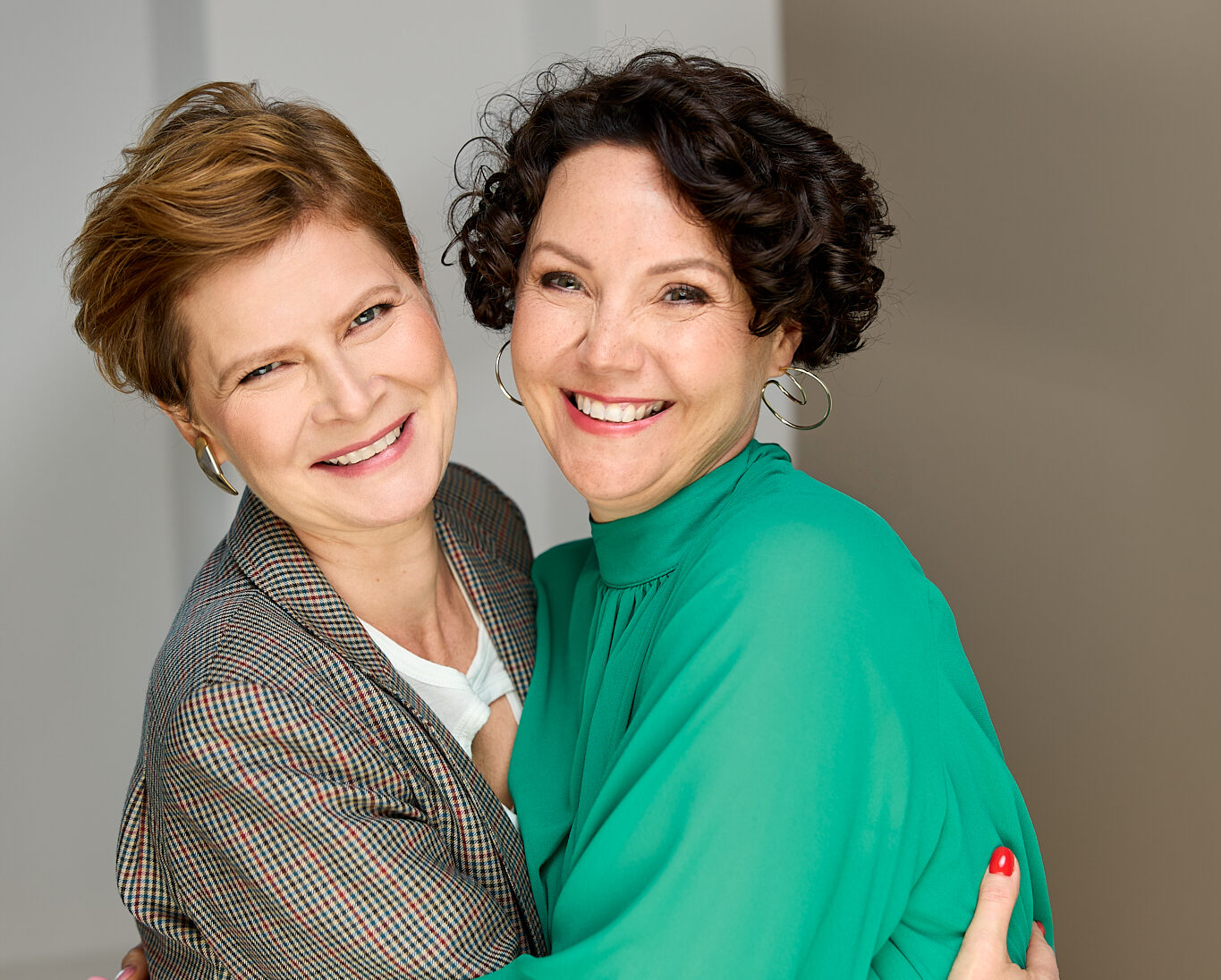 Dwie uśmiechnięte kobiety obejmują się i patrzą w stronę aparatu.