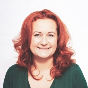 Uśmiechnięta kobieta o rudych, falowanych włosach na jasnym tle.