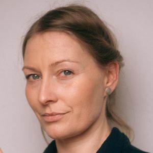 Kobieta z upiętymi włosami i delikatnym makijażem na tle jasnej ściany.