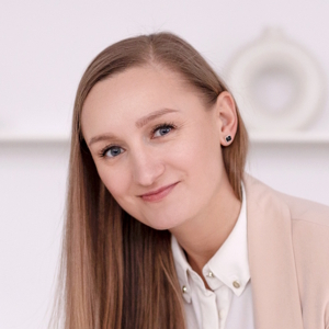 Młoda kobieta o długich prostych włosach w jasnej koszuli i marynarce uśmiecha się lekko.