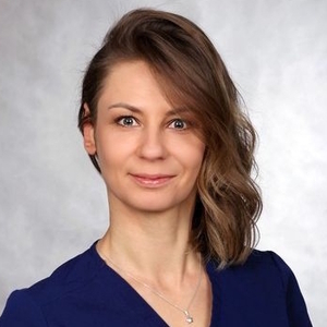 Kobieta o brązowych włosach do ramion w granatowej bluzce patrzy w obiektyw.