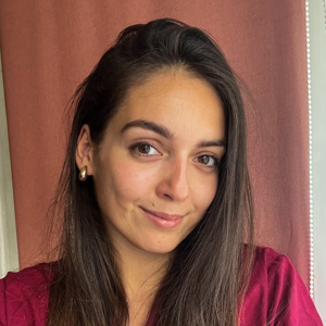 Młoda kobieta o długich ciemnych włosach w bordowej bluzce uśmiecha się lekko.