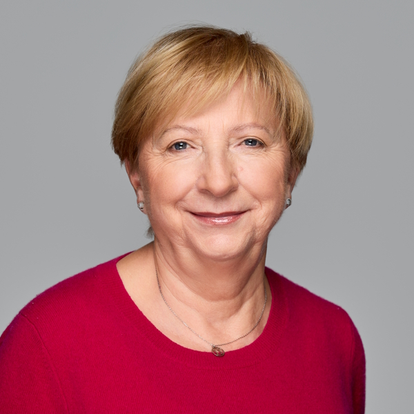 kobieta z krótkimi blond włosami w różowym swetrze na szarym tle.