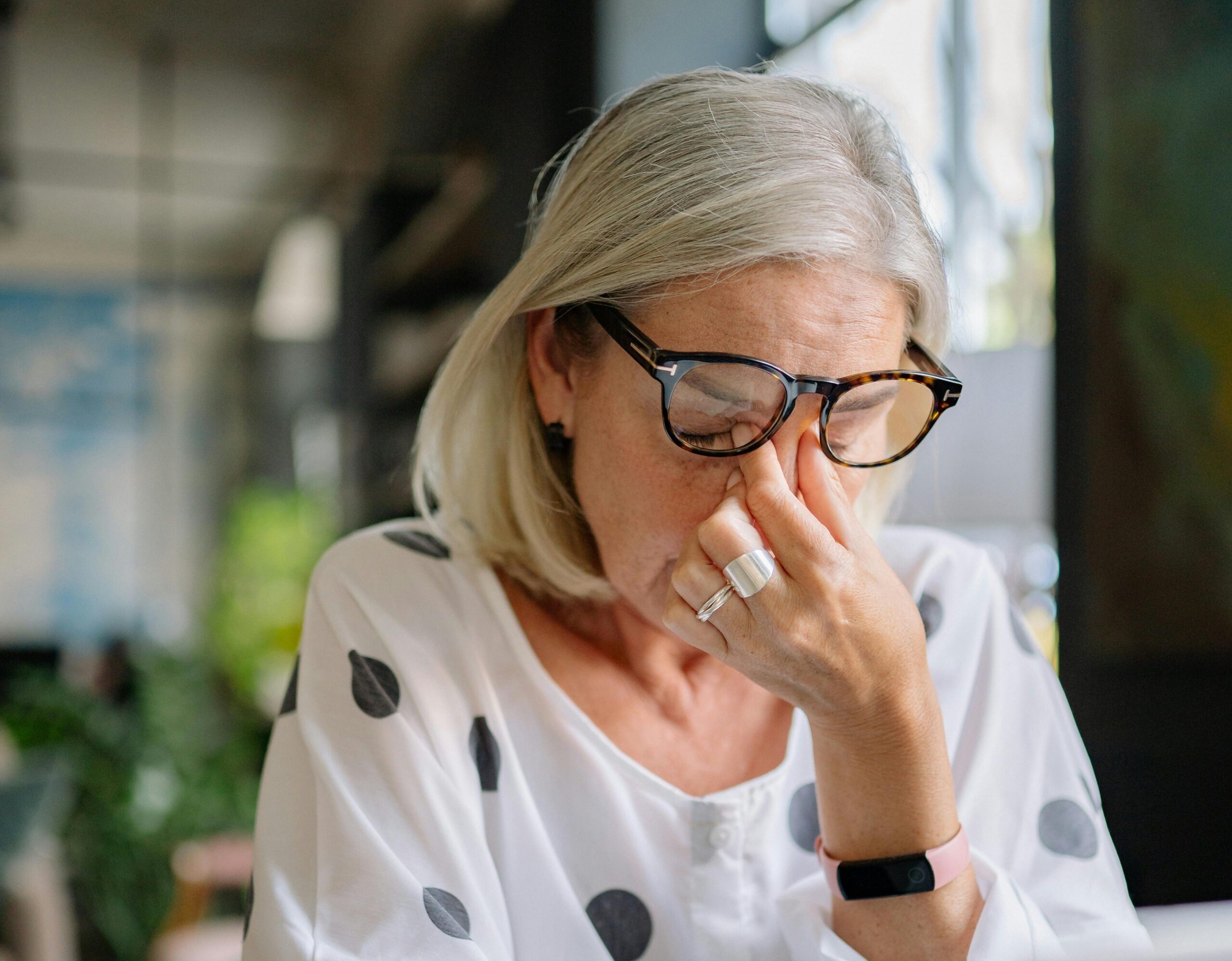 Kobieta w okularach zaciska palce na nasadzie nosa, wyglądając na zmęczoną.